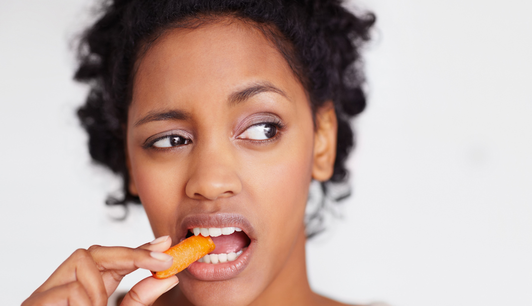 Unhappy woman eating a carrot